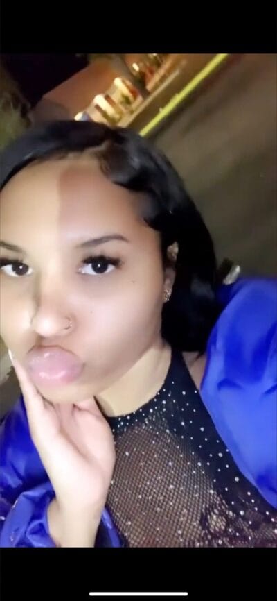 Close-up selfie of a woman making a kissing face at night, wearing a sparkly mesh top and blue jacket.