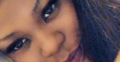 Close-up of a person with a warm smile, showing left eye and cheek, dark hair framing the face.