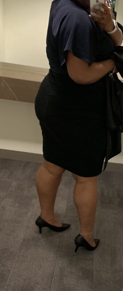 Person in a navy blouse and black pencil skirt, wearing black heels, taking a mirror selfie in a hallway.
