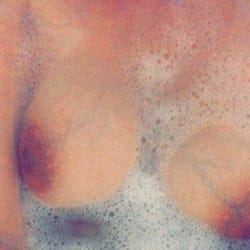 Two bare breasts partially covered in soap foam in a bathtub.