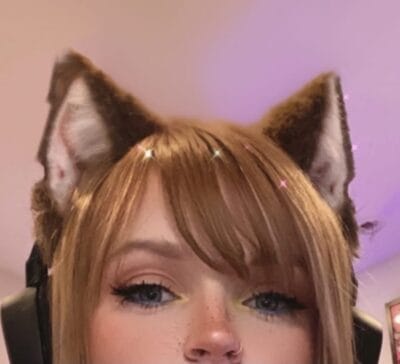 Close-up of a person wearing fluffy cat ears filter, with pink and purple lighting in the background.