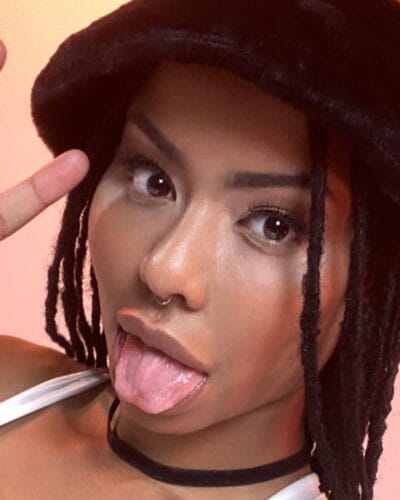 Close-up of a person sticking out their tongue while making a peace sign near their temple in a playful selfie.
