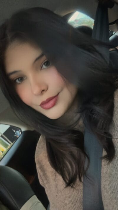 Portrait of a young woman with long dark hair wearing a seatbelt in a car, looking to the side.